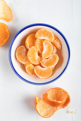 Slices of peeled tangerine in a bowl, top view. Close up of a mandarin orange over white background. 