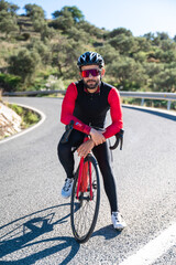 Cyclist posing with sunglasses, helmet and red and black uniform at the mountain. Looking the camera