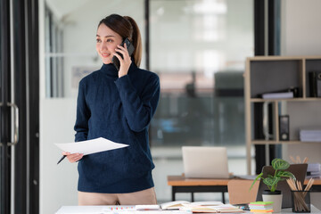 Image of an Asian businesswoman holding a document report and using a cellphone while working in an office