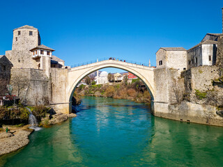 Fototapeta na wymiar Aerial drone view of the Old Bridge in Mostar city in Bosnia and Herzegovina during sunny day. Blue turquoise colors of Neretva river. Unesco World Heritage Site. People walking over the bridge.