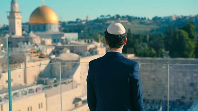 A bar mitzvah boy stands with his back to the camera on a balcony with a view of the Western Wall in the morning. Taking a beautiful video from a Bar Mitzvah ceremony.
