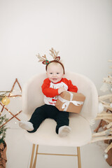 a little blond one-year-old boy unwraps a Christmas present. Christmas children's sweater.