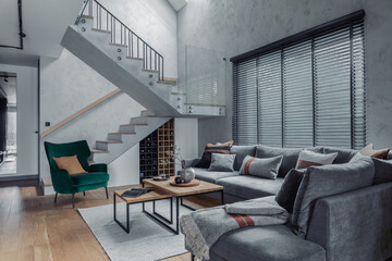 Stylish composition of modern living room design with corner grey sofa, green armchair, coffee table and minimalist personal accessories. Stairs in living room interior. Concrete walls. Template.