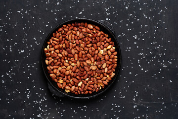 Roasted fresh peanuts in a frying pan on a black background with salt, close up.