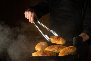 Oven baked buns on a hot baking sheet in the chef hand in glove. The chef takes a hot bun with a culinary tongs