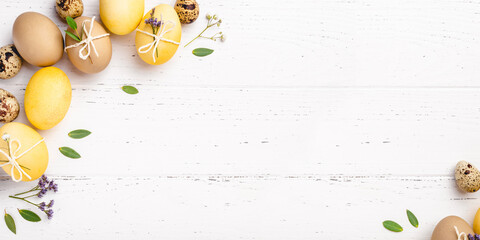 Festive Easter background. Yellow and brown Easter eggs with flowers on a white table. Banner with a place for text.