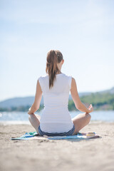 Junge Frau beim Meditieren am Strand von einem italienischen See im Sommer