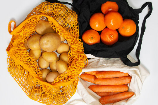 Fresh farm vegetables and fruits. Reusable shopping bags. Fabric bag, mesh bag, string bag. Filled with vegetables and fruits. Potatoes, carrots, tangerines, oranges. View from above. 