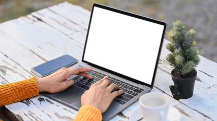 Fototapeta premium Close up view of young female freelancer hands typing on laptop computer while sitting at outdoor cafe