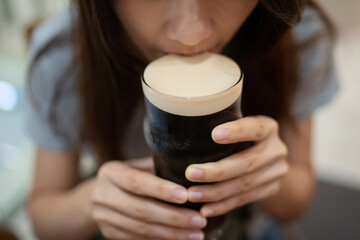 Asian lady holding the glass with one hand and sipping the foam of the nitro cold brew coffee