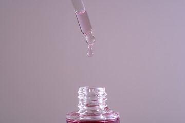 Pink face oil drop from glass pipette dropper. Macro close up for cosmetic neutral background...