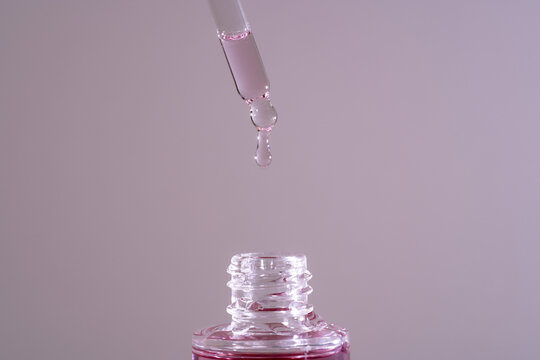 Pink face oil drop from glass pipette dropper. Macro close up for cosmetic neutral background bakuchiol hyaluronic serum with fig extract