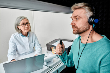 Male patient wearing audiology headphones pressing button of response while audiometric testing in...