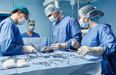 Group of concentrated surgeons while surgical operation in operating theater, side view. Teamwork in surgical department