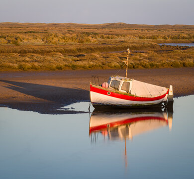 Red and white fishing boat at low tide with reflection at Burnham Overy Staithe, Norfolk