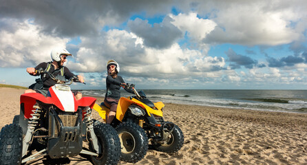 Quad driving people - happy smiling couple bikers in sand beach. North Sea, Denmark.