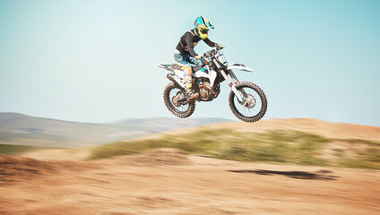 Motorcycle, offroad driving and air jump in desert, blue sky and freedom. Driver, cycling and power stunt on dirt track, competition and motorbike performance on adventure course for fast action show