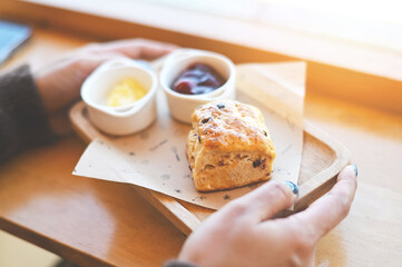 scones and jam on wooden plate, woman served scones and cream for dessert and tea - fresh homemade butter scones