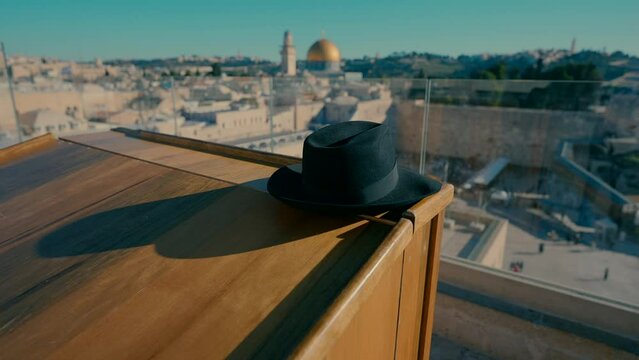A black Orthodox hat rests on the wooden table in the balcony with a view of the Western Wall in the morning.