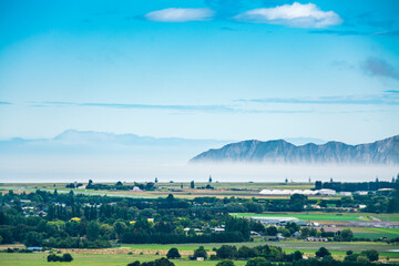 Mist rising over distant mountain range in the the sea not far from green mainland. Gisborne, North...