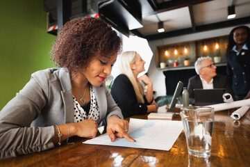 Close-up latin young businesswoman or student sitting at desk analyzing data. Team work at background.