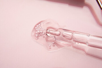 Pipette with a cosmetic transparent product on a pink background.