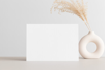 White invitation card mockup with a dried flower on the beige table. 5x7 ratio, similar to A6, A5.