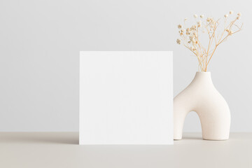 Square invitation card mockup with a gypsophila decoration  on the beige table. 