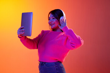 Greetings. Young girl in headphones having online video call on tablet over gradient orange...