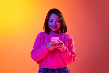 Conversation. Young girl in pink sweater typing text message on mobile phone over gradient orange...