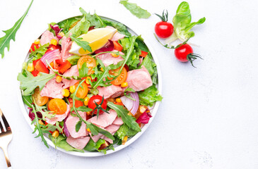 Tuna vegetables salad with colorful cherry tomatoes, red onion, sweet corn, paprika, lettuce, radicchio and arugula. White table background, top view