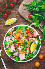 Fresh tuna vegetables salad with colorful cherry tomatoes, red onion, sweet corn, paprika, lettuce, radicchio and arugula. Rustic wood table background, top view