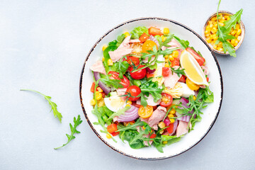 Tuna vegetables salad with cherry tomatoes, red onion, eggs, corn, paprika, lettuce, radicchio and arugula. Gray table background, top view