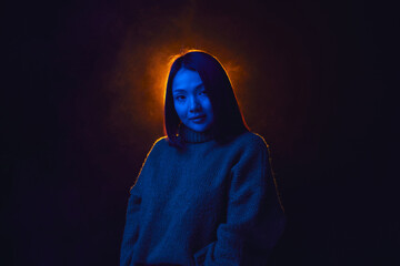 Fototapeta na wymiar Young girl, student in cozy sweater over dark background in blue neon light with smoke effect. Concept of emotions, facial expression, lifestyle, youth, inspiration, sales, ad