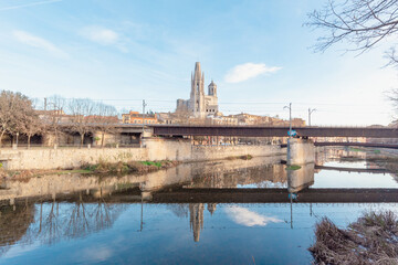 Puente para cruzar por encima del río caminando  y entrar a la ciudad de Gerona bajo un día soleado y cálido con el reflejo de la catedral en el río.