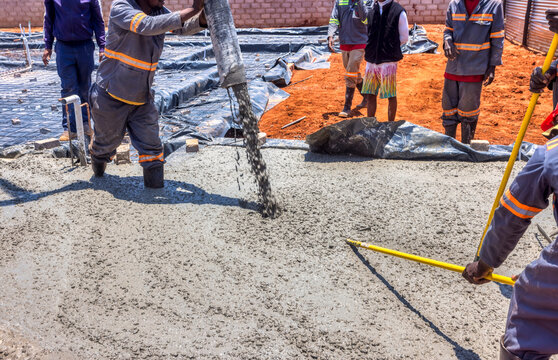 african construction workers using a boom concrete pump to fill the foundation of a building