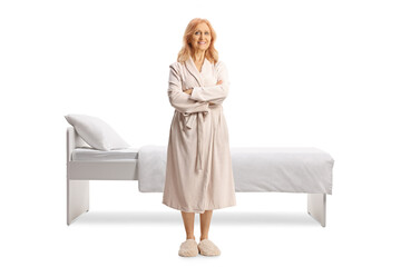 Full length portrait of a mature woman in a bathrobe standing in front of a bed