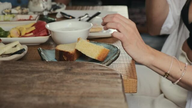 Manos de mujer partiendo un trozo de bizcocho con las manos y comi&eacute;ndoselo en una mesa de desayuno. 