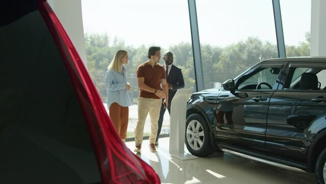 African American salesperson demonstrating new crossover model to ethnically diverse couple in modern car showroom