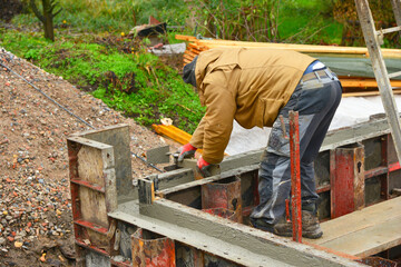 Bauarbeiter beim Glattstrich der Mauerkrone mit der Kelle an einer mit der Betonpumpe gegossenen...