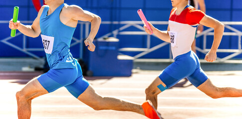 two male athletes with relay baton in hands run at competition