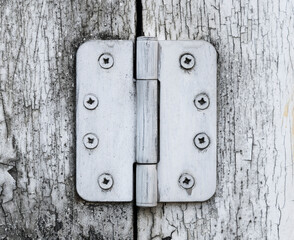 Old and worn big heavy white painted metal hinge against a worn wooden door.