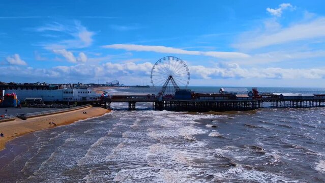 pier overhead view. Birds flying on the Ferris wheel and the pier. Waves crashing on the shore in the blue sea