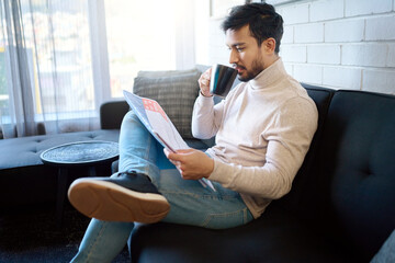 Relax and reading newspaper by man with coffee or drinking tea in a home, house or apartment on weekend. Mexican, news and young person enjoying free time with an article, story or paper