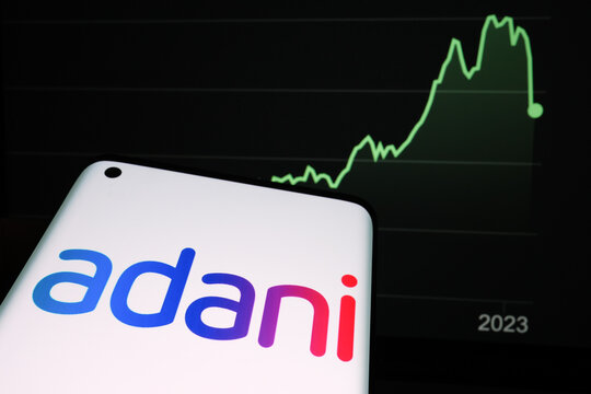 Adani Group logo seen on the smartphone screen and company stock price drop graph seen on the blurred background. Real stock chart for a year timeframe. Stafford, United Kingdom, February 2, 2023