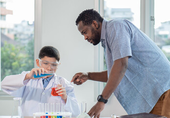 Teacher and child student studying chemical science in classroom. Multiracial male tutor teaching liquid experiment to boy pupil in class. Schoolboy back to school and learning with multiethnic person