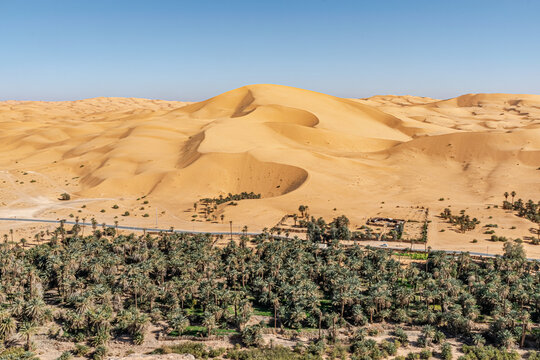 Taghit town of Bechar, Algeria Sahara desert. Palm trees oasis, a khaima or a tuareg stable dome tent covered with mats and sand dune with a blue clear sky. Aerial view from Djebel Baroun mountain.