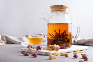 Glass teapot of hot fragrant craft blossom tea with cup and dry rose bud, sugar