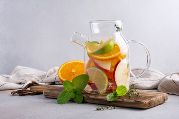 Glass teapot for healthy fruit tea with fresh ripe citrus, apples, mint and thyme