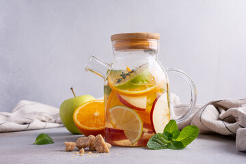 Glass teapot of hot healthy sweet fruit tea with fresh ripe citrus, apples, mint and thyme
